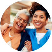 Caregiver and elderly woman smiling together outdoors.