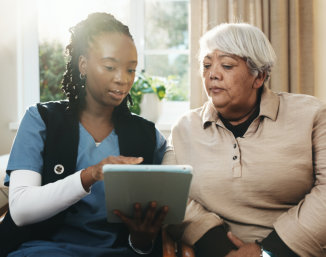 Caregiver showing an elderly woman information on a tablet.