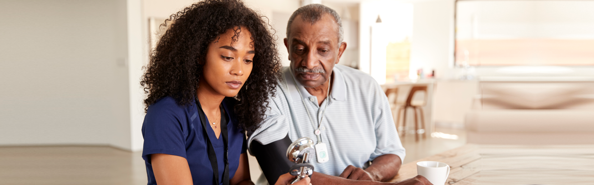 Caregiver checking an older man's blood pressure at home.
