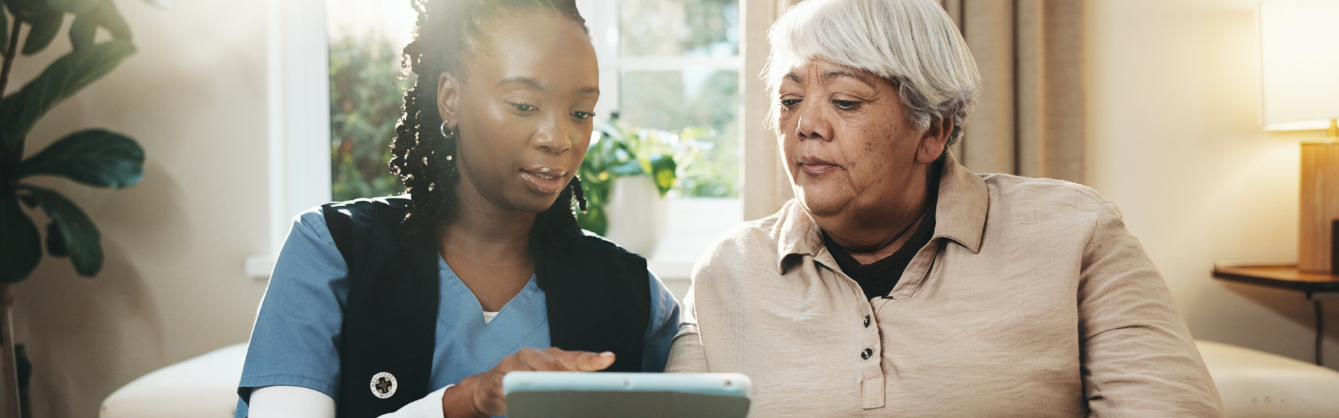 Caregiver showing an elderly woman information on a tablet.